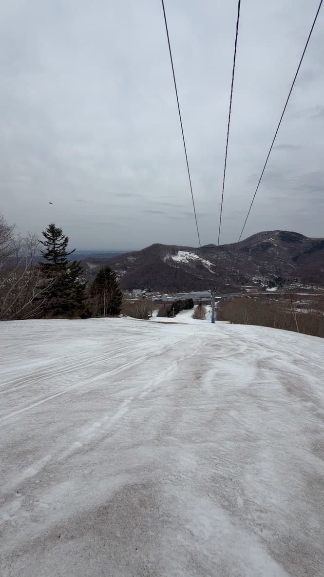 A ski run on Mount Racey under a winter sky, chairlift cables overhead and the valley below.